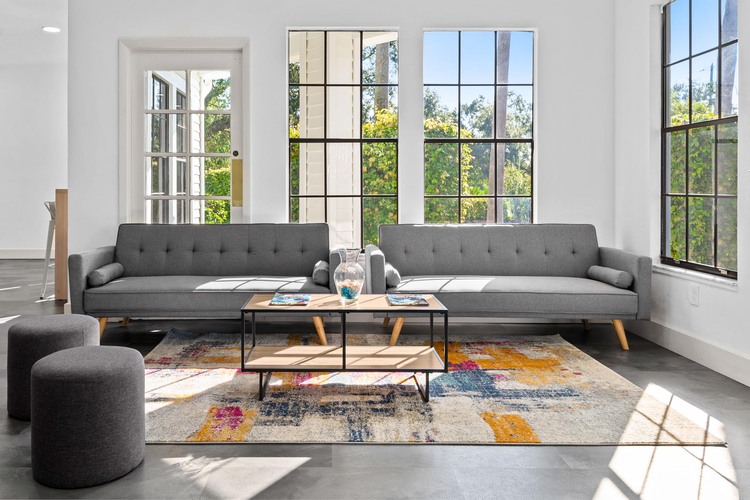 Dos sofás grises, una mesa de madera con un jarrón de vidrio y ventanas grandes y luminosas