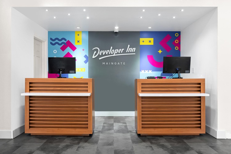 Two wooden desks with computer terminals and Developer Inn Maingate sign on wall